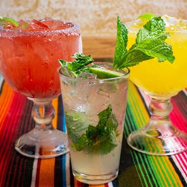 Three colorful cocktails, two margaritas and one mojito, on a vibrant striped serape tablecloth.