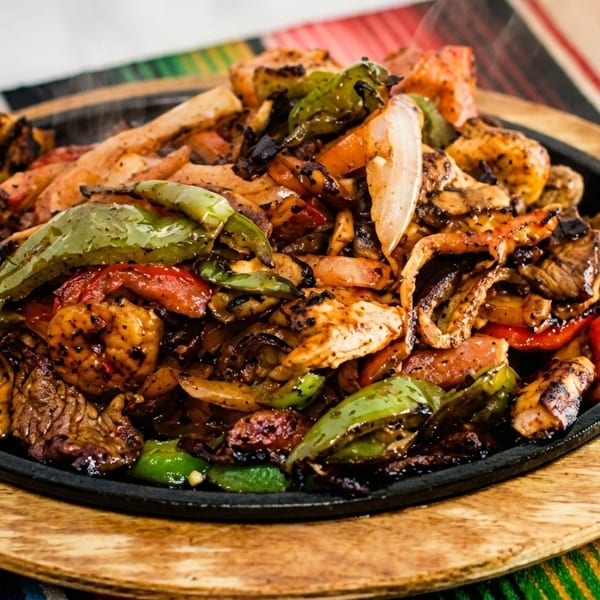 Sizzling fajitas with steak, chicken, shrimp, peppers, and onions on a cast iron skillet.