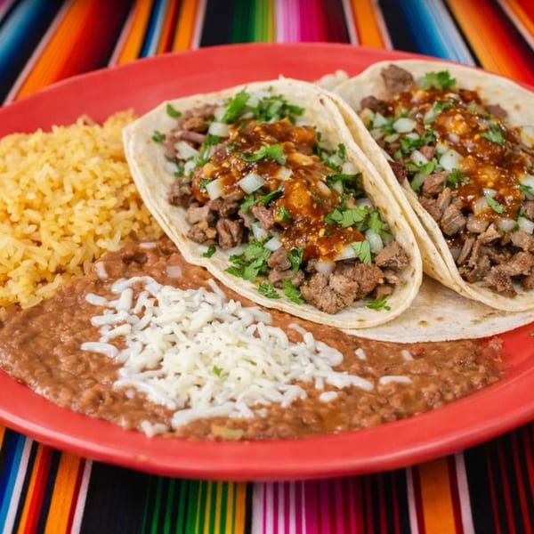 Two carne asada tacos with rice and refried beans on a red plate, on a colorful striped tablecloth.
