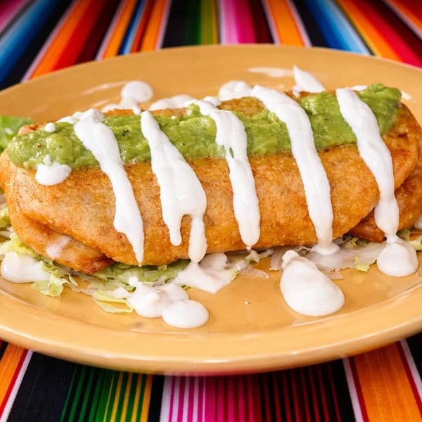 Golden-fried chimichanga topped with guacamole and sour cream, served on a yellow plate.