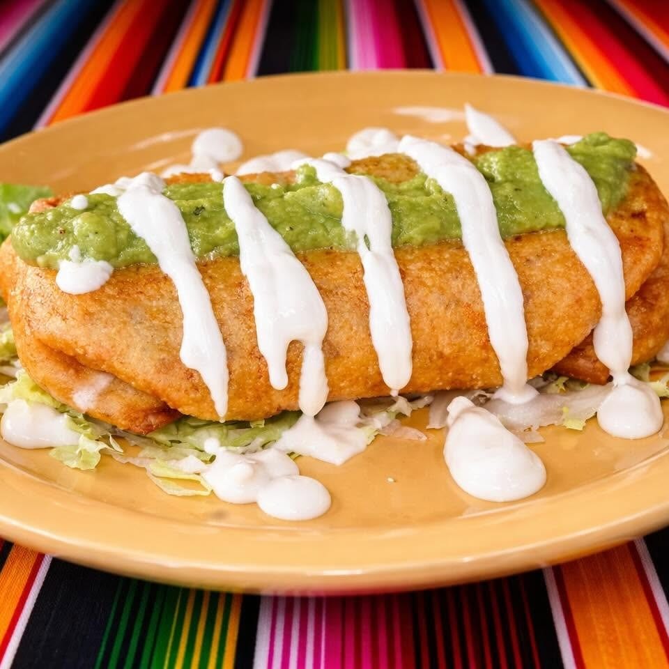 Golden-fried chimichanga topped with guacamole and sour cream, served on a yellow plate.