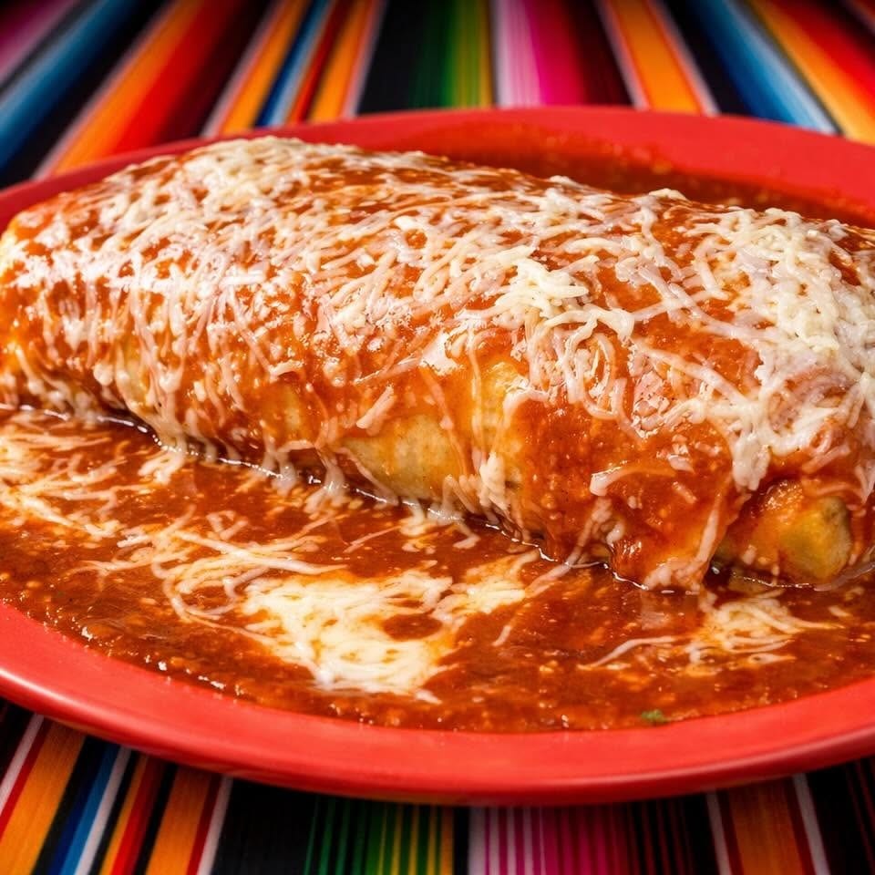 A large, smothered burrito covered in red sauce and melted cheese on a red plate.